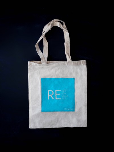 Saco tote branco com estampa azul e textos, sobre fundo preto.