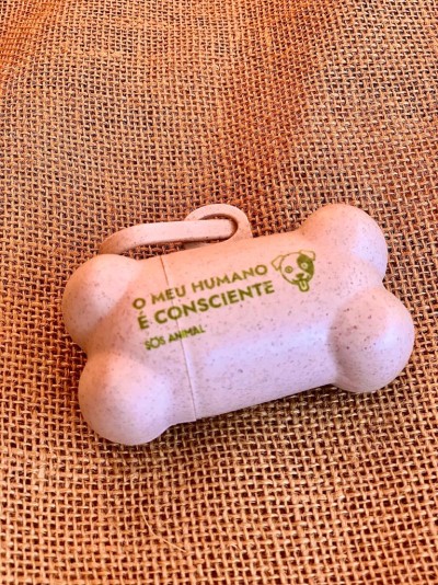 Dispenser bege em forma de osso para sacos com inscrição verde colocado sobre tecido de juta