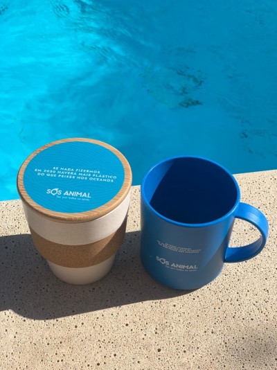 Caneca azul e copo reutilizável branco com mensagem ambiental ao lado de uma piscina
