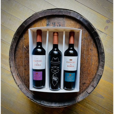 Três garrafas de vinho embaladas em caixa branca sobre barril de madeira