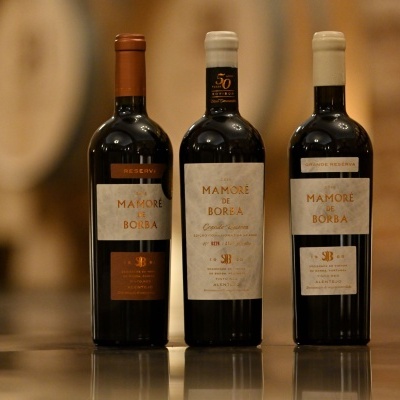 Três garrafas de vinho Madiró de Borba com rótulos brancos e detalhes dourados em ambiente rústico