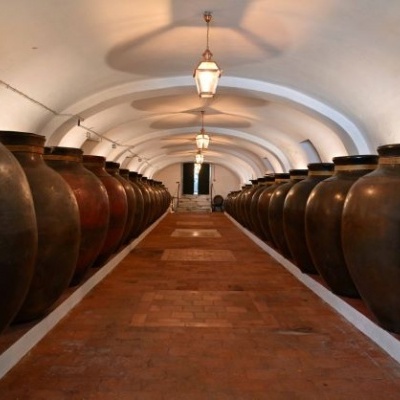 Corredor com grandes jarros de cerâmica castanhos e pretos em filas, chão de tijolos e teto arqueado branco