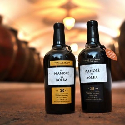 Duas garrafas de vinho Mamoré de Borba com rótulos amarelo e preto em adega com barris ao fundo