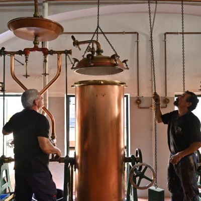 Equipamentos industrial de destilação em cobre com duas pessoas operando