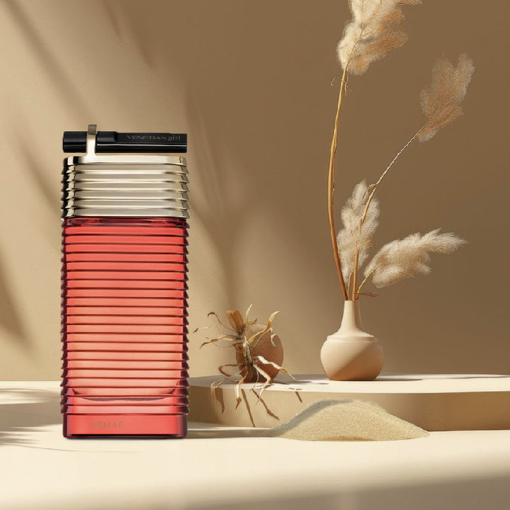 Frasco de perfume YVES SAINT LAURENT vermelho e preto sobre superfície clara com vasos e plantas secas