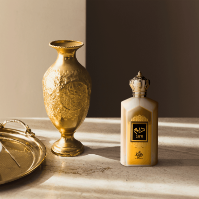 Frasco de perfume dourado com vaso dourado decorativo e tabuleiro sobre superfície de pedra