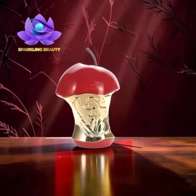 Frasco de perfume em forma de metade de maçã vermelha e dourada sobre superfície de madeira