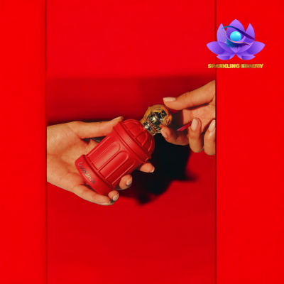 Frasco vermelho de perfume em forma de hidrante com tampa dourada nas mãos de uma pessoa, fundo vermelho.