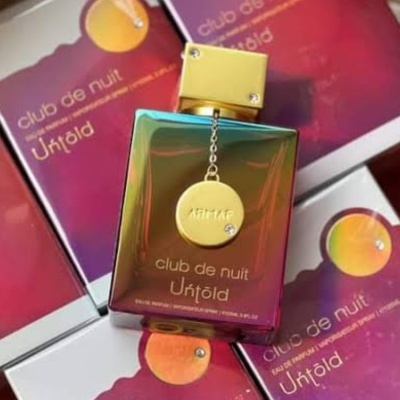 Frasco de perfume tornassol com tampa dourada e pendente, rodeado por caixas roxas com gradiente laranja