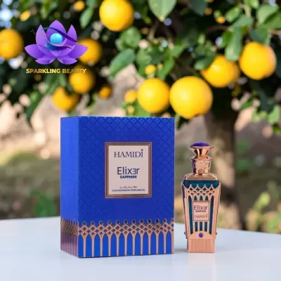 Frasco e embalagem do perfume concentrado Hamidi Elixer Sapphire azul e dourado sobre mesa branca com árvores de limão ao fundo