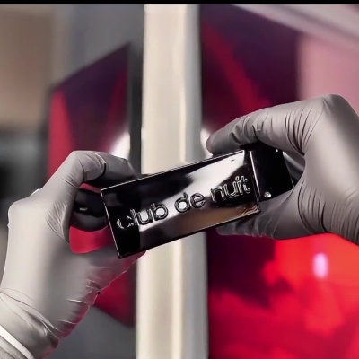 Foto de uma mão com luva segurando uma garrafa preta de perfume Armaf Club de Nuit