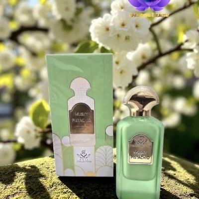 Frasco de perfume verde pistácio com tampa dourada ao lado da sua caixa verde clara em ambiente natural com flores brancas
