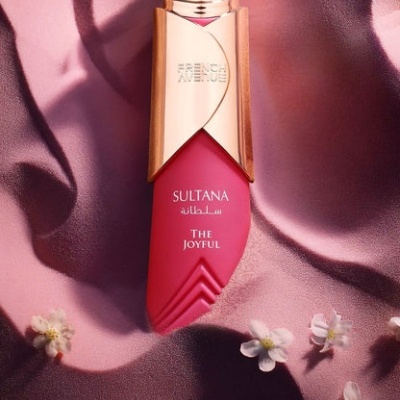 Frasco de perfume rosa e dourado com tampa em forma de coroa e texto SULTANA THE JOYFUL FRENCH AVENUE.