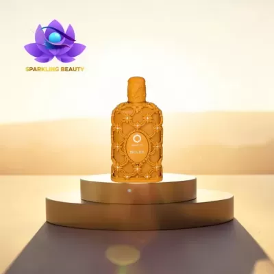 Frasco de perfume laranja com relevo decorativo floral e pedras sobre plataforma dourada