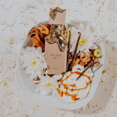 Frasco dourado de perfume com flores, nozes e chantili numa tigela branca