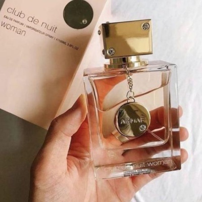 Frasco de perfume transparente com tampa dourada e embalagem branca ao fundo.