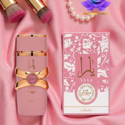 Perfume Yara da Lattafa com embalagem rosa e dourada numa superfície de tecido rosa com pincéis e colar de pérolas