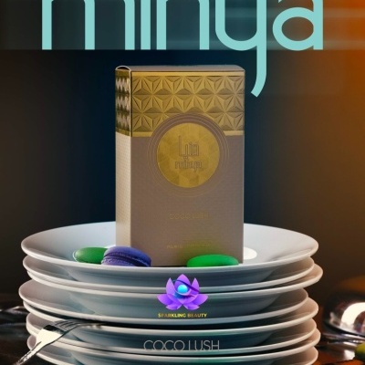 Caixa dourada com padrão e texto Les mitrajes sobre pratos brancos empilhados com macarons verdes e roxos.