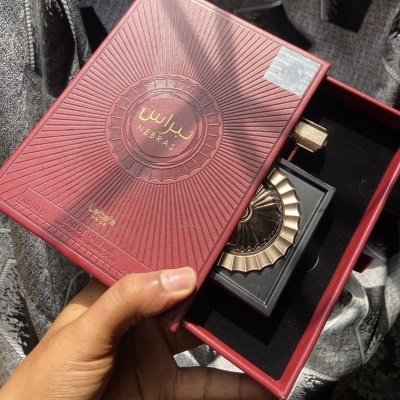 Caixa de perfume vermelha com frasco preto e tampa dourada em fundo cinzento