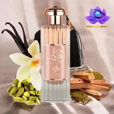 Frasco de perfume com tampa dourada e borla preta, flores e especiarias ao redor