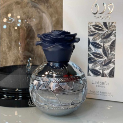 Frasco prateado de perfume com tampa azul e embalagem branca com padrão de folhas