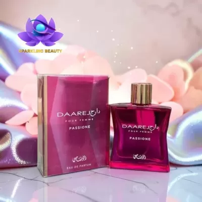 Frasco e caixa de perfume vinho DAAREJ Passione sobre superfície branca com tecidos rosados e lilás ao fundo.