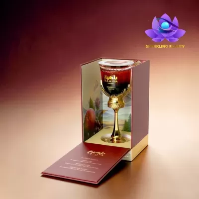 Frasco de perfume Bahiya Garnet em copo dourado com líquido vermelho na caixa aberta de cartão bordeaux.
