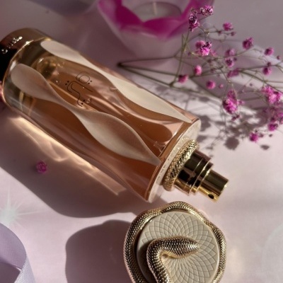 Frasco de perfume rosado com tampa decorada por serpente dourada e flores pequenas rosas