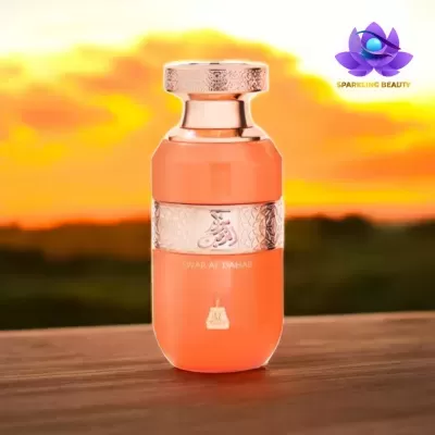 Frasco de perfume cor de pêssego com detalhes metálicos dourados sobre mesa de madeira e pôr-do-sol ao fundo