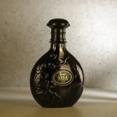 Frasco de perfume preto com design em relevo e rótulo dourado 'NYLA SUEDE'