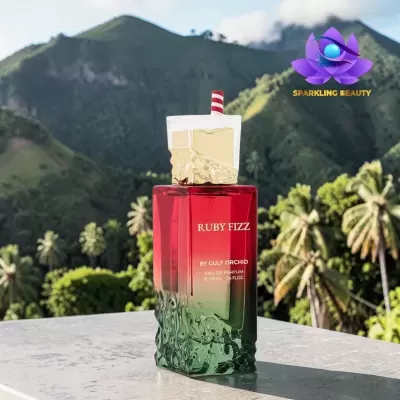 Frasco de perfume Ruby Fizz em vidro vermelho e verde com tampa dourada, montanhas e palmeiras ao fundo