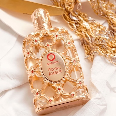 Frasco de perfume dourado com ornamentos vermelhos e texto ORIENTICA ROYAL AMBER