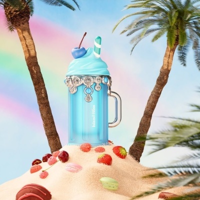 Caneca azul translúcida com chantili decorativo azul e palha listrada sobre areia com frutas e macarrons