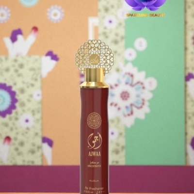 Frasco de perfume vermelho AJWAA com tampa dourada decorativa sobre mesa com fundo floral colorido