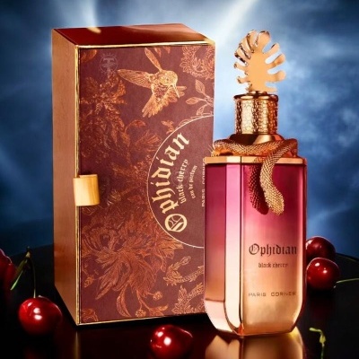 Frasco de perfume rosa escuro com tampa dourada e caixa castanha ao lado, rodeado de cerejas