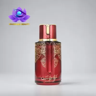 Frasco de perfume vermelho com decoração dourada e tampa vermelha sobre fundo cinzento