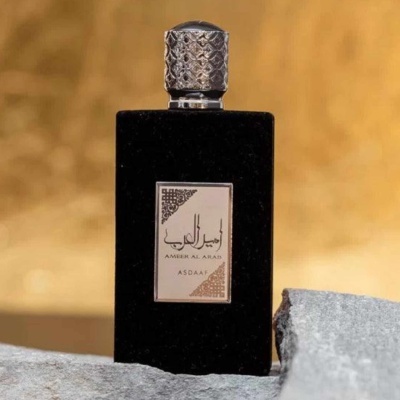 Frasco de perfume preto com tampa prateada e etiqueta em árabe sobre pedra