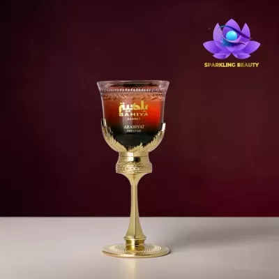 Frasco de perfume dourado e vermelho em taça sobre superfície branca