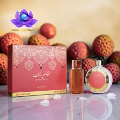 Conjunto de perfumaria Lychee Musk com frascos e caixa vermelha, detalhes dourados, sobre mesa refletiva com frutos litchi ao fundo