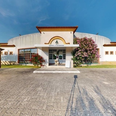 Fachada branca de edifício com telhado de telha vermelha e entrada com toldo branco