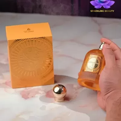 Frasco de perfume laranja e caixa com padrão circular num fundo de mármore claro