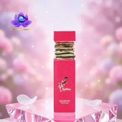 Frasco rosa de perfume Habiba com tampa dourada sobre base translúcida e fundo rosa desfocado