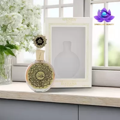 Frasco de perfume redondo com padrões dourados e pretos, em frente a uma embalagem branca, junto a flores brancas e janela