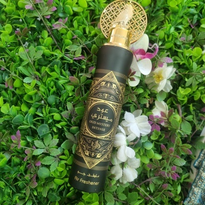 Spray aromatizador de ar preto com design dourado sobre plantas e flores