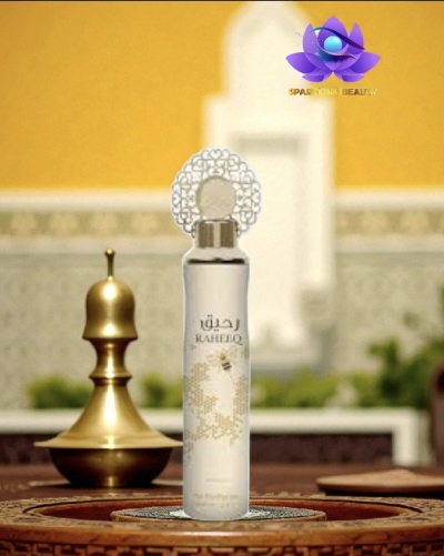 Frasco translúcido branco com texto RAHREEQ e tampa decorativa ao lado de objeto dourado em superfície de madeira