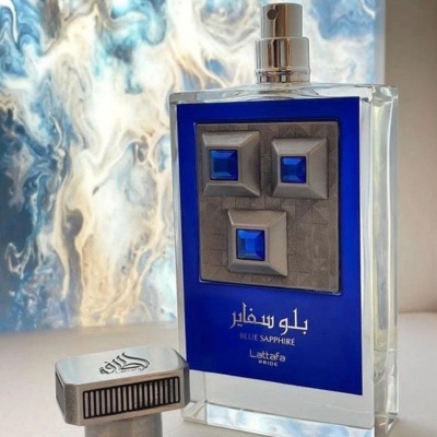 Frasco de perfume azul com detalhes em azul escuro e tampa metálica perto de superfície brilhante azul e branca