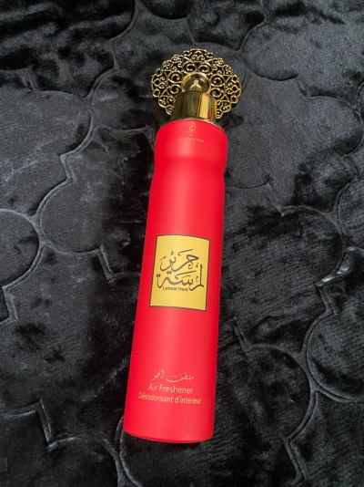 Ambientador vermelho com tampa dourada e etiqueta amarela sobre superfície preta