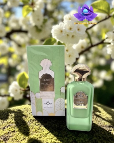 Frasco de perfume verde pistácio com tampa dourada ao lado da sua caixa verde clara em ambiente natural com flores brancas