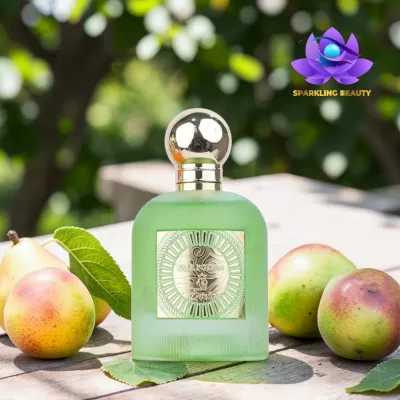 Frasco de perfume verde fosco com tampa metálica redonda e etiquetas douradas junto a peras sobre mesa em exterior