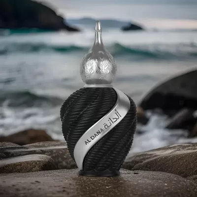 Frasco de perfume preto texturizado com tampa prateada sobre rochas junto ao mar